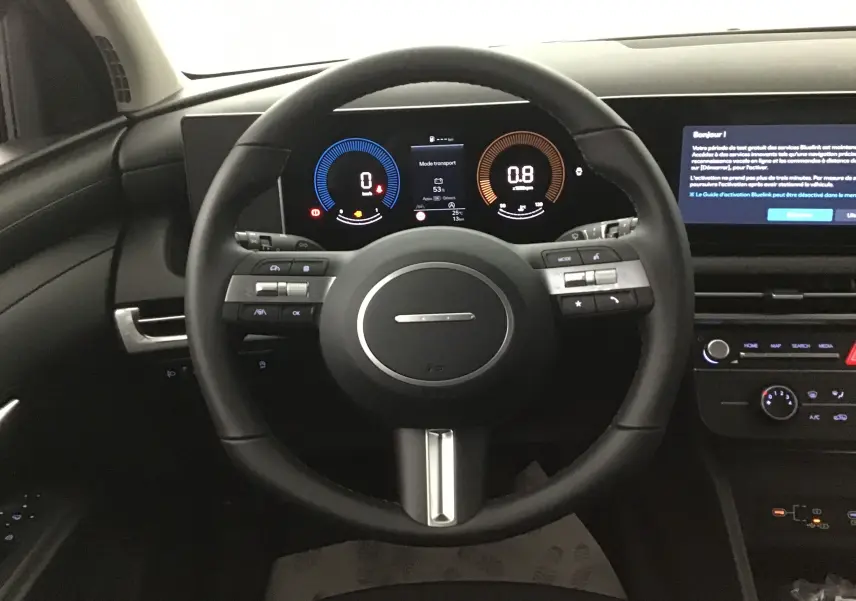 Vue intérieure centrée sur le volant cuir du Hyundai Tucson 2025 avec tableau de bord numérique et écran tactile.