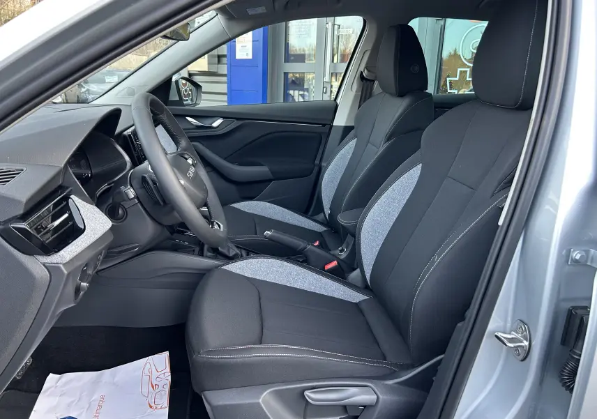 Vue intérieure côté gauche du Skoda Kamiq gris argent métal 2025, mettant en valeur les sièges tissu bicolores noirs et gris.