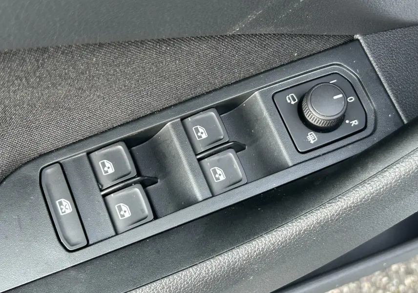 Gros plan sur les commandes de lève-vitres et réglage des rétroviseurs côté conducteur d’un Skoda Kamiq gris argent.