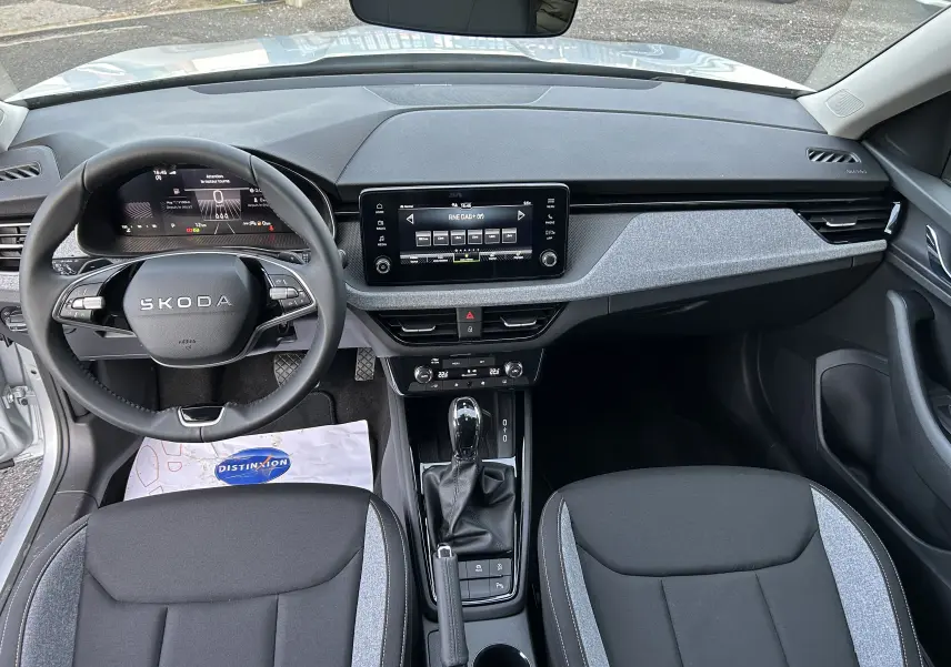 Vue intérieure avant du Skoda Kamiq 2025, tableau de bord gris noir avec écran tactile et volant multifonction.