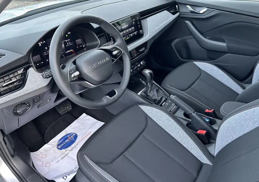 Vue intérieure côté conducteur de la Skoda Kamiq 2025 avec sellerie tissu gris et noir et tableau de bord moderne.