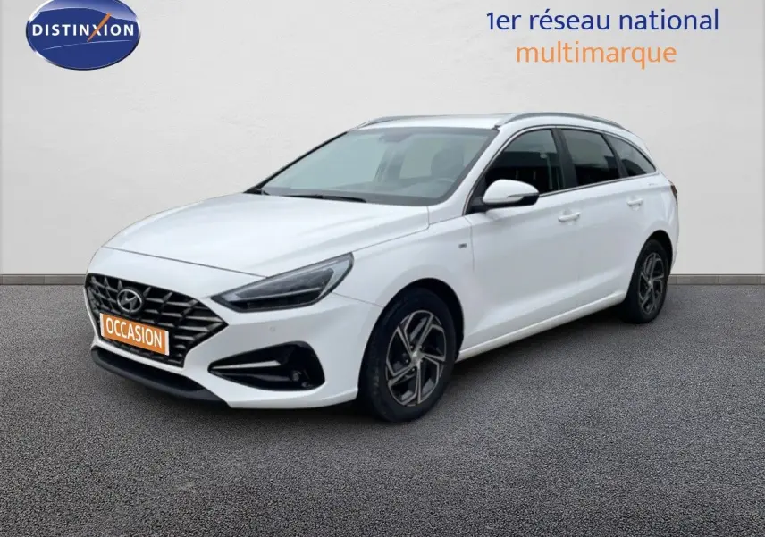 Vue 3/4 avant droit d'une Hyundai i30 SW blanche Atlas avec calandre noire et jantes alliage distinctives.