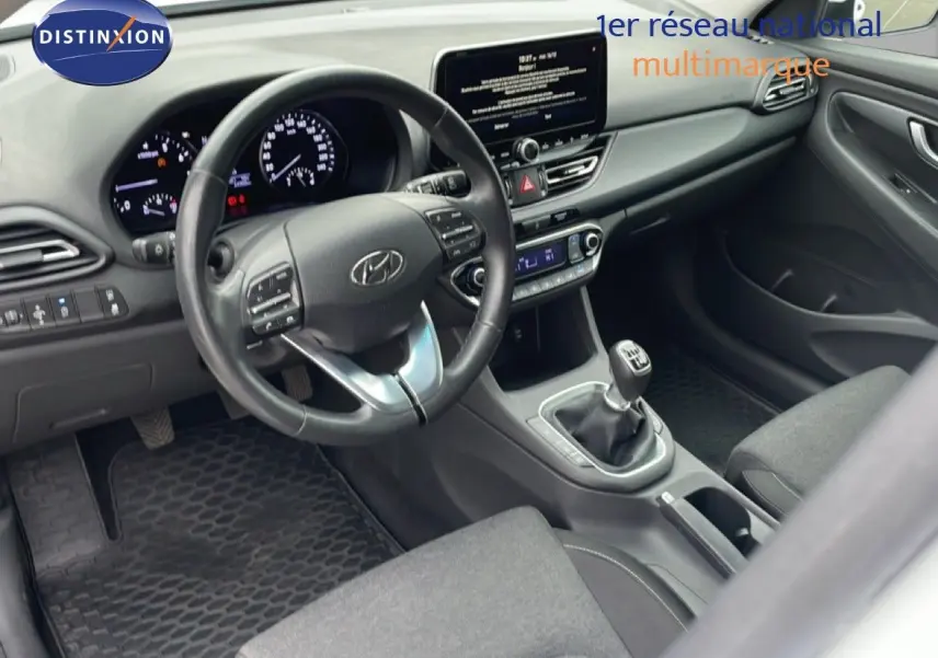 Vue intérieure côté conducteur de la Hyundai i30 SW 2023, tableau de bord moderne avec écran tactile et boîte manuelle.