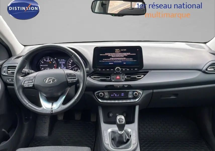 Vue intérieure frontale du tableau de bord et volant noir de la Hyundai i30 SW 2023 avec écran tactile et boîte manuelle.