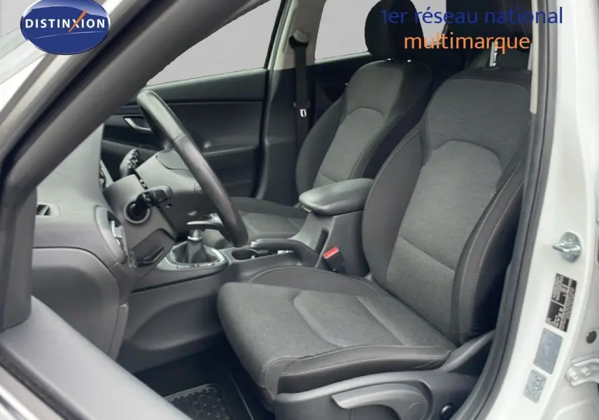 Intérieur côté conducteur de la Hyundai i30 SW blanc Atlas 2023, sièges tissu gris et volant cuir noir.