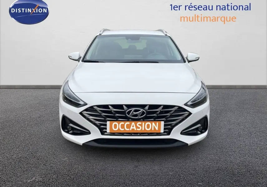 Vue frontale d'une Hyundai i30 SW 1.5 T-GDI 160CH FAMILY SMART blanche avec calandre noire et feux LED.