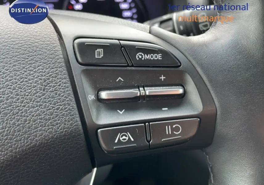 Gros plan sur les commandes au volant noir du Hyundai i30 SW 2023, avec boutons de mode et régulateur de vitesse.