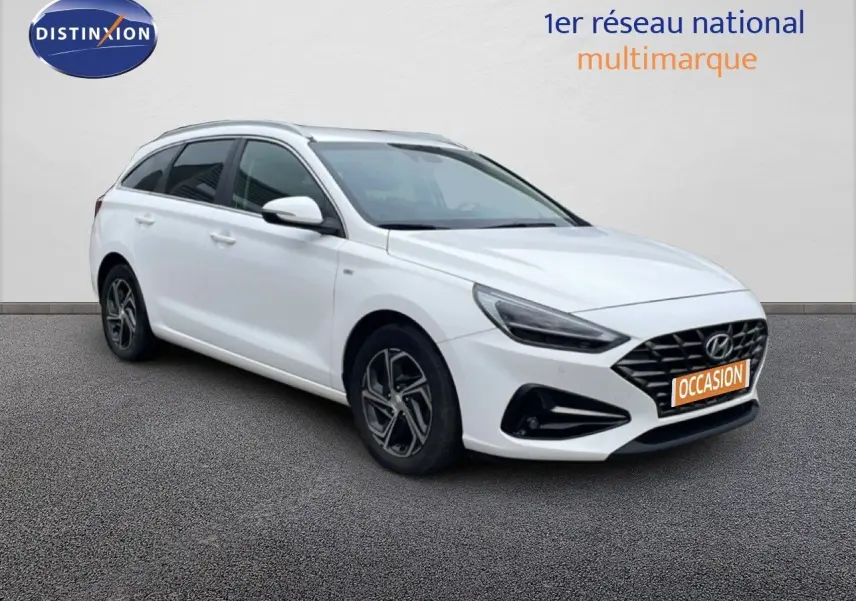 Vue 3/4 avant droit d'une Hyundai i30 SW blanche avec calandre noire et jantes alliage distinctives.