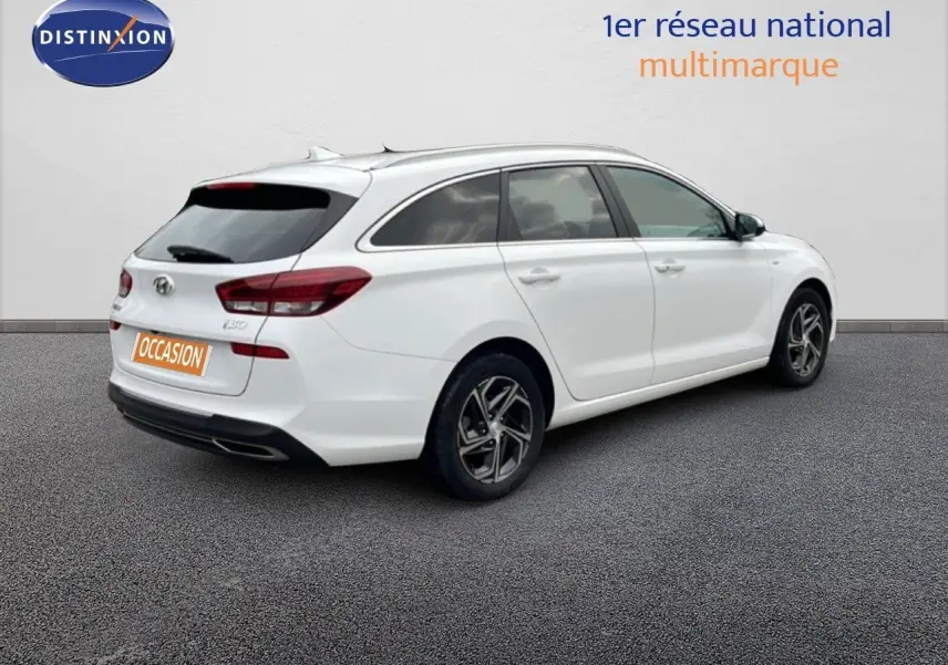 Vue 3/4 arrière droite d'une Hyundai i30 SW blanche Atlas avec jantes alliage et vitres teintées.