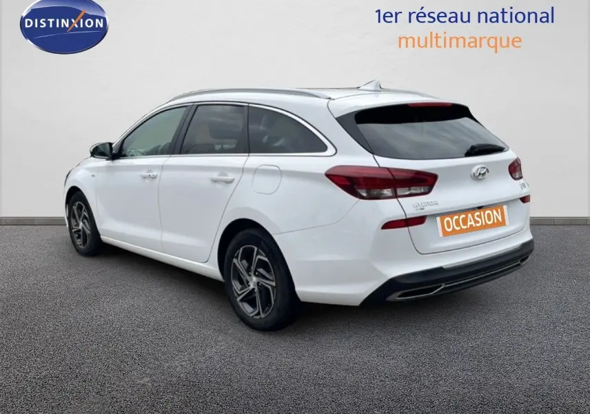 Vue 3/4 arrière droite d'une Hyundai i30 SW blanche Atlas avec jantes alliage et vitres teintées.