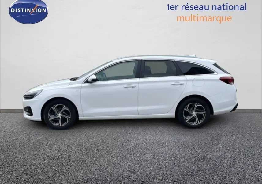 Profil latéral droit d'une Hyundai i30 SW 2023 blanche Atlas, break compact avec jantes alliage et vitres teintées.
