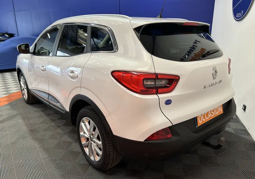 Vue 3/4 arrière droite d’un Renault Kadjar blanc 2018 avec attelage et vitres arrière teintées en showroom.