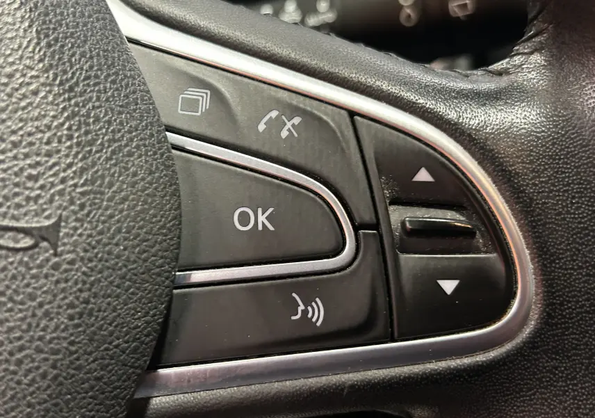 Gros plan sur les commandes multifonctions noires du volant en cuir d’un Renault Kadjar blanc de 2018.