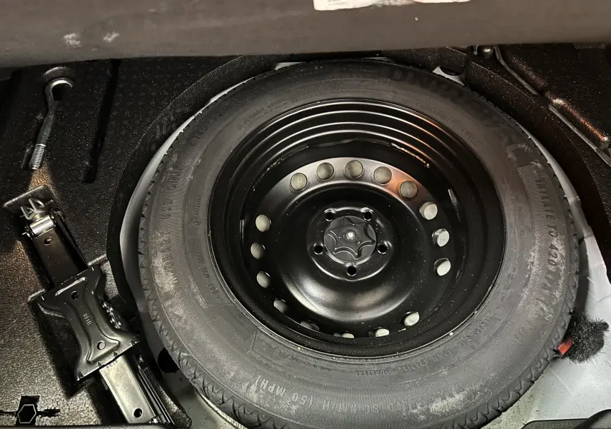 Gros plan sur la roue de secours noire et le cric dans le coffre d’un Renault Kadjar blanc de 2018.