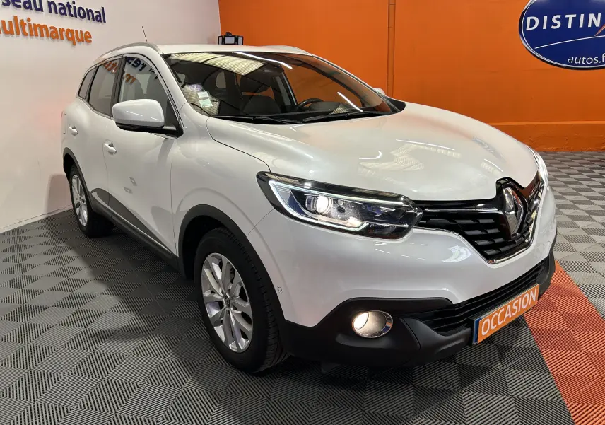 Renault Kadjar blanc en 3/4 avant droit, phares allumés, avec attelage visible et plaque "OCCASION" devant.
