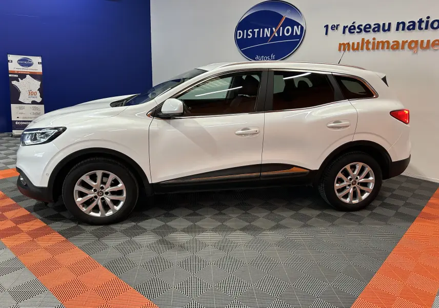 Vue latérale droite d'un Renault Kadjar blanc 2018 en showroom, avec jantes alliage et attelage visible à l'arrière.
