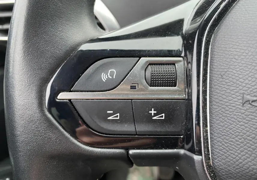 Gros plan sur les commandes de volume et de fonction vocale du volant noir du Peugeot 3008 gris platinium 2021.