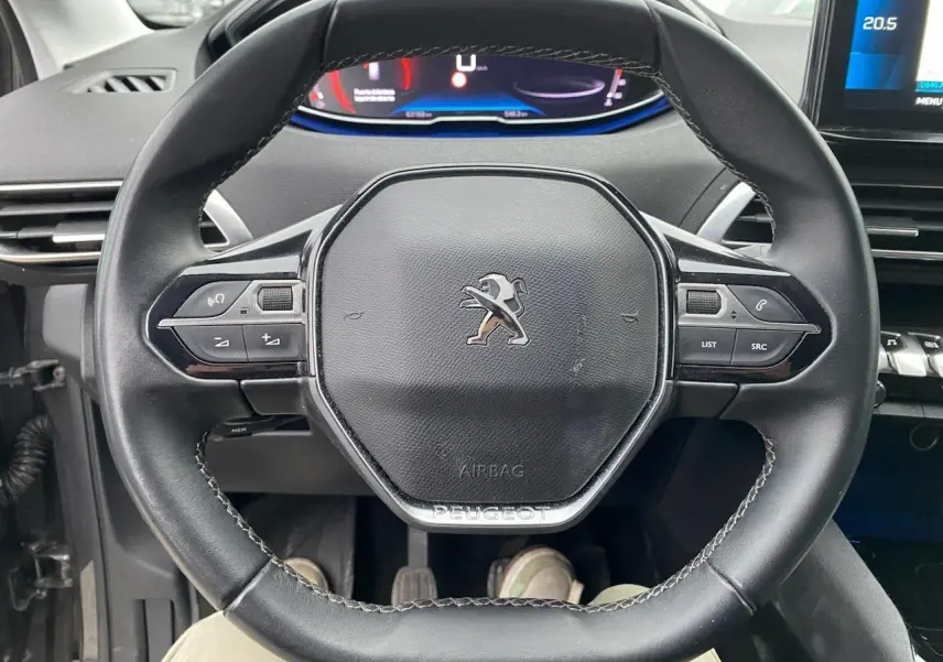 Vue rapprochée du volant compact noir du Peugeot 3008 2021 avec commandes multifonctions et combiné numérique en arrière-plan.