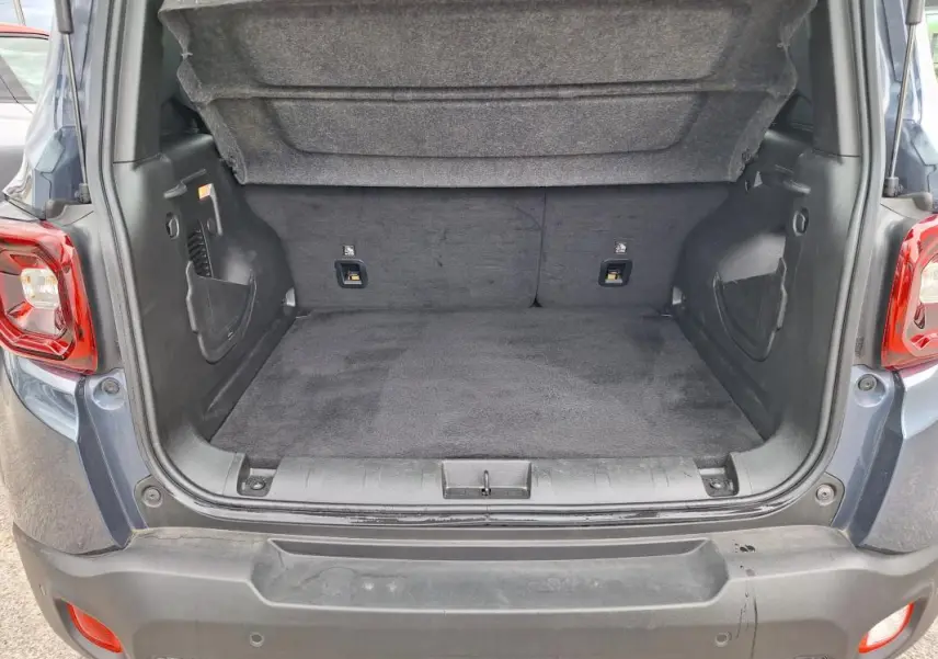 Coffre ouvert vu de l'arrière d'un Jeep Renegade bleu 2024, montrant l'espace de chargement vide et la moquette noire.