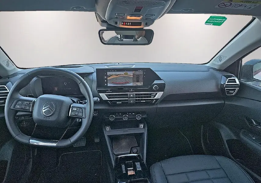 Vue intérieure avant du Citroën C4 X 1.2 hybride 2025, tableau de bord noir avec écran tactile et volant multifonctions.