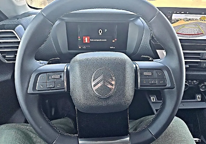 Vue centrée sur le volant cuir noir de la Citroën C4 X 1.2 hybride, avec tableau de bord numérique et écran de caméra de recul.
