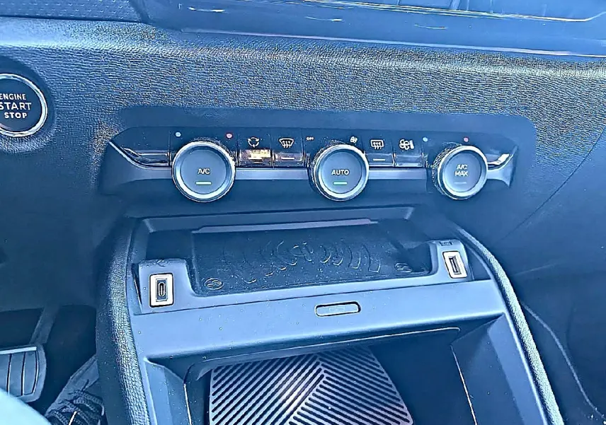 Vue rapprochée de la console centrale noire du Citroën C4 X 1.2 hybride, montrant les commandes de climatisation et prises USB.