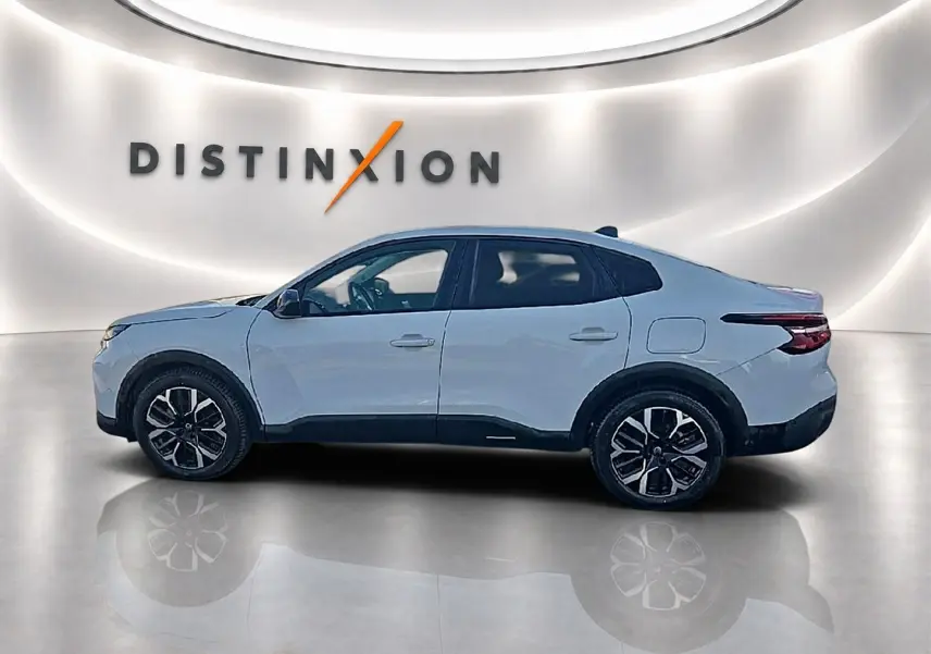 Vue de profil côté gauche d'une Citroën C4 X blanche 2025 avec jantes alu noires et toit noir dans un showroom.