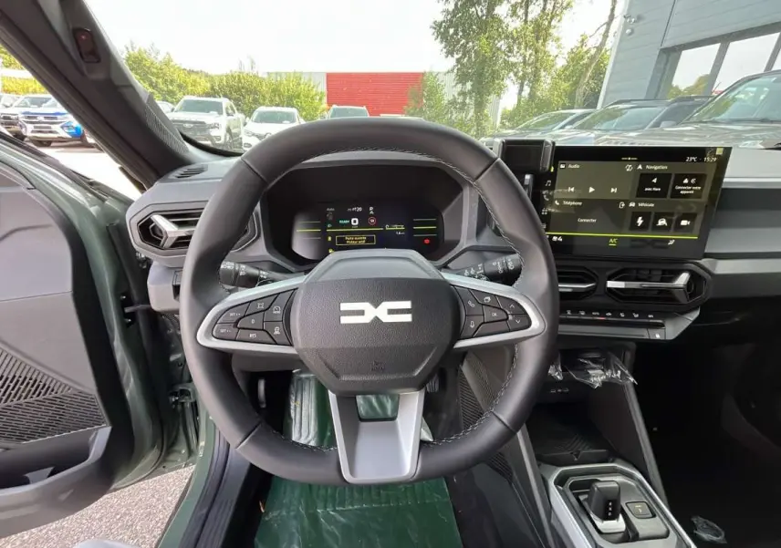 Vue intérieure centrée sur le volant et tableau de bord du Dacia Duster Hybrid-G 150 4x4 en kaki lichen, avec écran tactile.