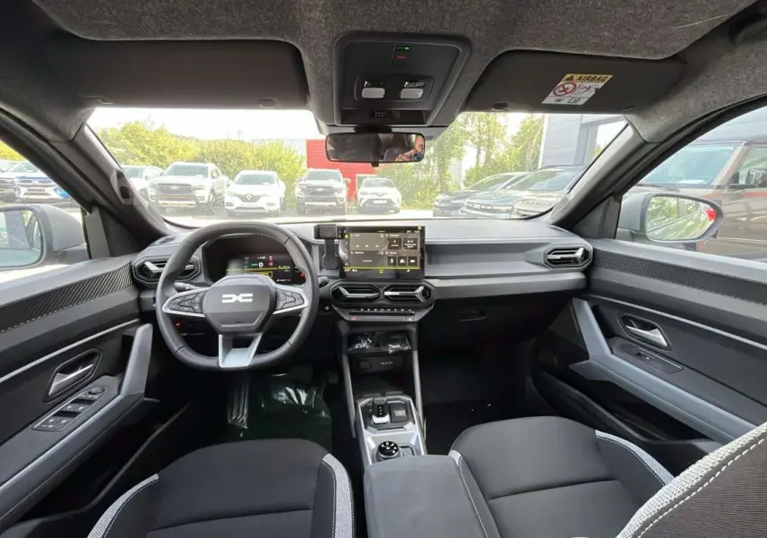 Vue intérieure avant du Dacia Duster Hybrid-G 150 4x4 Journey City, tableau de bord moderne et sièges noirs.