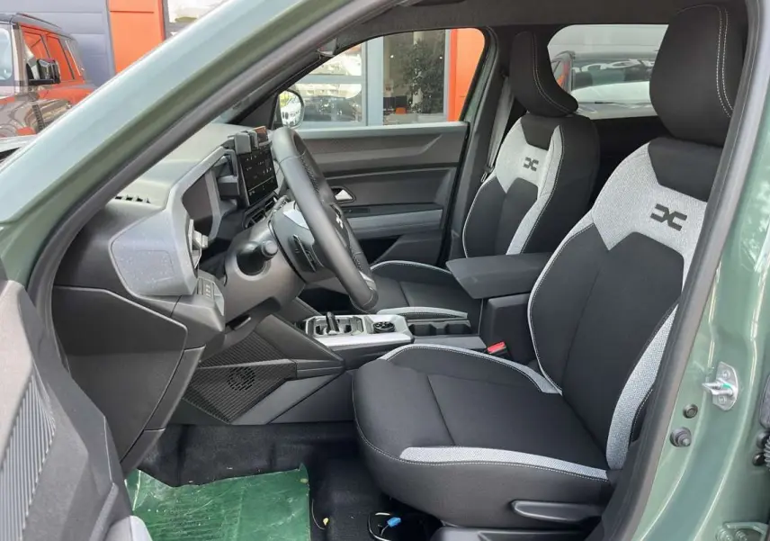 Vue intérieure côté conducteur du Dacia Duster 2026 kaki lichen, avec sièges bi-ton et accoudoir central avant.
