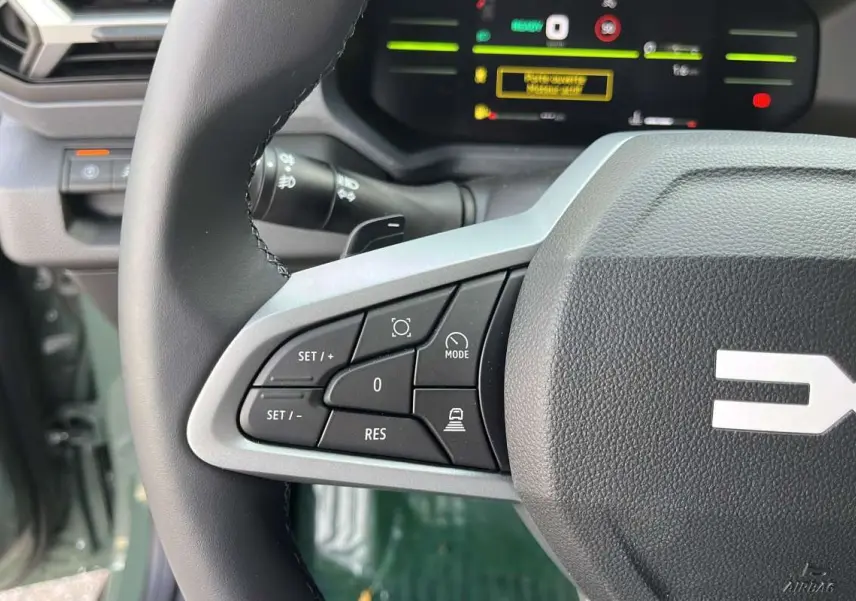 Gros plan sur le volant cuir du Dacia Duster Hybrid-G 150, montrant les commandes de régulateur et d'aide à la conduite.