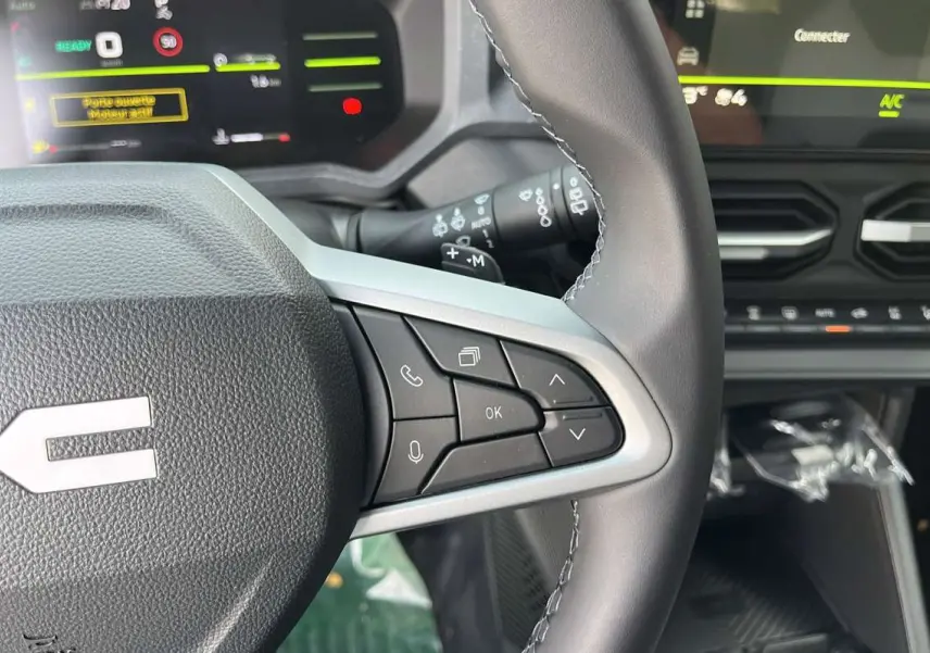 Gros plan sur le volant cuir du Dacia Duster 2026 avec commandes multifonctions et tableau de bord numérique en arrière-plan.