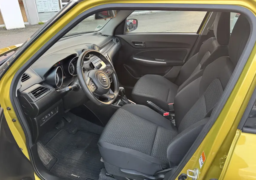 Intérieur côté conducteur d'une Suzuki Swift 1.2 Pack Auto 2023 jaune/gris, avec sièges noirs et tableau de bord moderne.