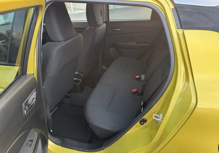 Vue intérieure arrière gauche d'une Suzuki Swift 1.2 Pack Auto 2023 jaune/gris, montrant les sièges arrière noirs et la porte ouverte.