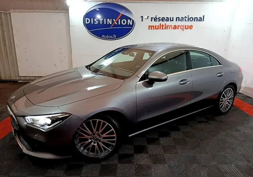 Vue 3/4 avant droit d'une Mercedes CLA 180 d Business Line gris clair avec jantes alliage et phares allumés en intérieur.