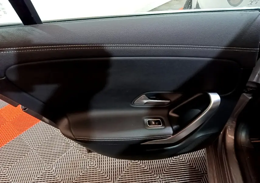 Vue intérieure côté gauche de la porte noire de la Mercedes CLA 180 d Business Line avec poignée argentée et bouton de vitre électrique.