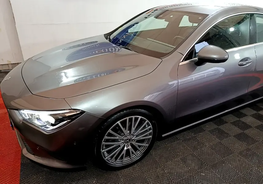 Mercedes Classe CLA 180 d gris clair vue 3/4 avant droit avec jantes alliage et phares LED allumés.