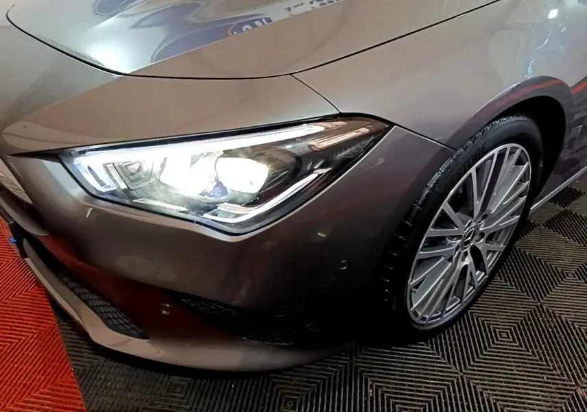 Gros plan sur l'avant droit gris clair d'une Mercedes CLA 180 d Business Line avec phare LED allumé et jante alliage.