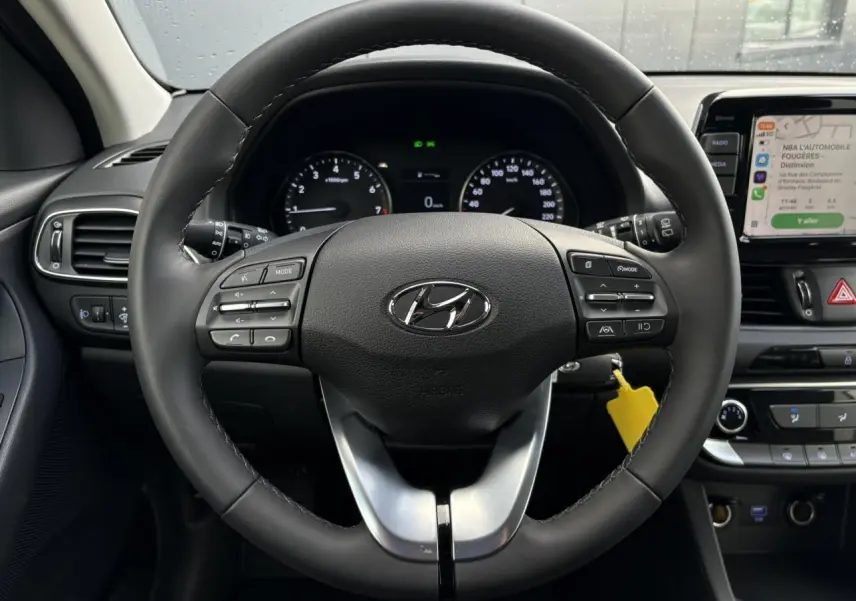 Vue rapprochée du volant cuir noir de la Hyundai i30 SW 2025 avec commandes intégrées et écran tactile multimédia.