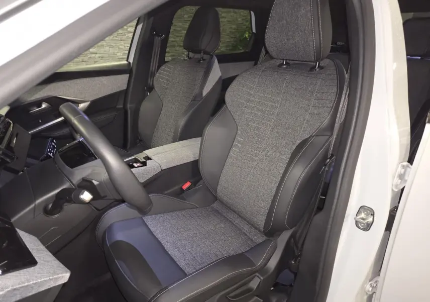 Vue intérieure côté conducteur du Peugeot 5008 blanc 2025, sièges tissu gris et cuir noir avec surpiqûres.