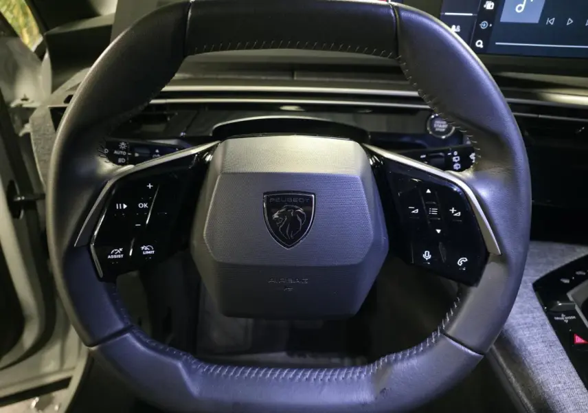 Gros plan sur le volant noir du Peugeot 5008 2025 avec logo lion et commandes intégrées, intérieur moderne.