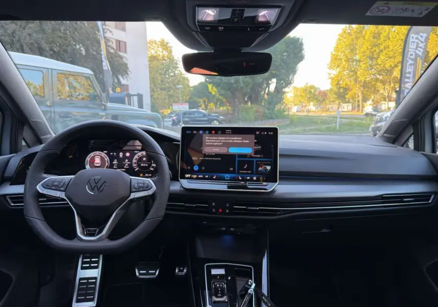 Vue intérieure avant de la Volkswagen Golf gris argent avec volant multifonctions et écran tactile central allumé.