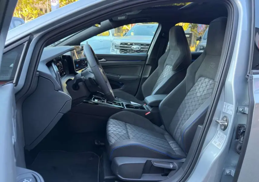 Intérieur de la Volkswagen Golf E-TSI 150 R-Line 2026, vue côté conducteur, sièges sport gris avec surpiqûres bleues.