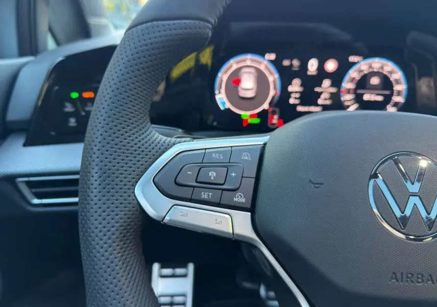 Gros plan sur le volant multifonctions en cuir de la Volkswagen Golf E-TSI, avec tableau de bord numérique en arrière-plan.