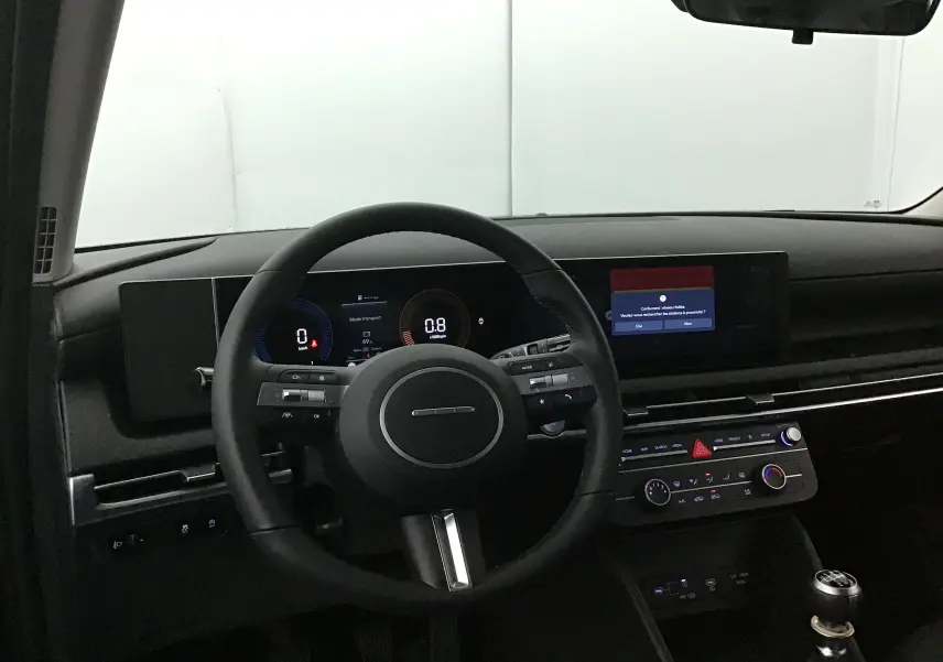 Intérieur du Hyundai Tucson 2025, vue du poste de conduite avec volant cuir, tableau de bord numérique et levier de vitesse manuel.