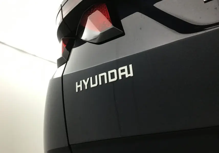 Gros plan sur le logo Hyundai à l'arrière d'un Tucson bleu Salling, avec feux arrière anguleux visibles en partie.