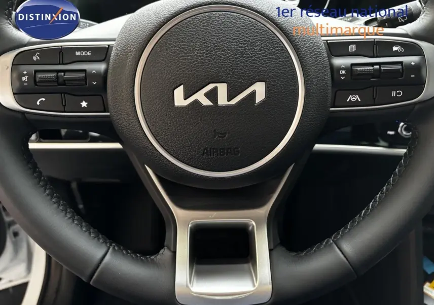 Gros plan sur le volant cuir noir du Kia Sportage 2025, mettant en valeur les commandes intégrées et le logo central.