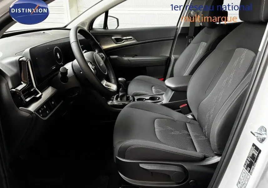 Vue intérieure côté conducteur du Kia Sportage blanc nacré, mettant en valeur les sièges noirs et la console centrale avec boîte manuelle.