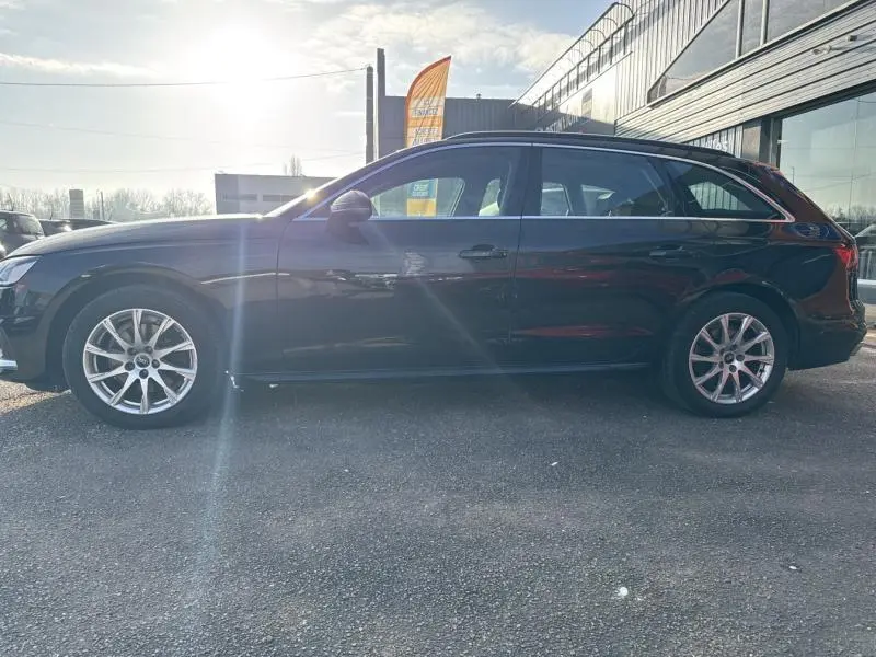 Profil côté gauche d'une Audi A4 Avant noire brillante de 2022, avec jantes alu et barres de toit visibles.
