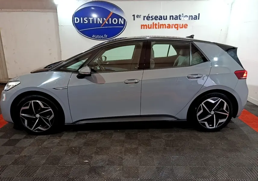 Vue de profil côté gauche d'une Volkswagen ID.3 77 kWh Pro S gris foncé avec jantes noires et argentées, en intérieur showroom.